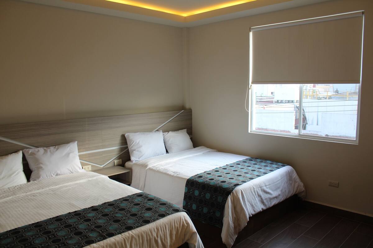 Habitación de hotel con dos camas, un ventanal grande y vistas al exterior.