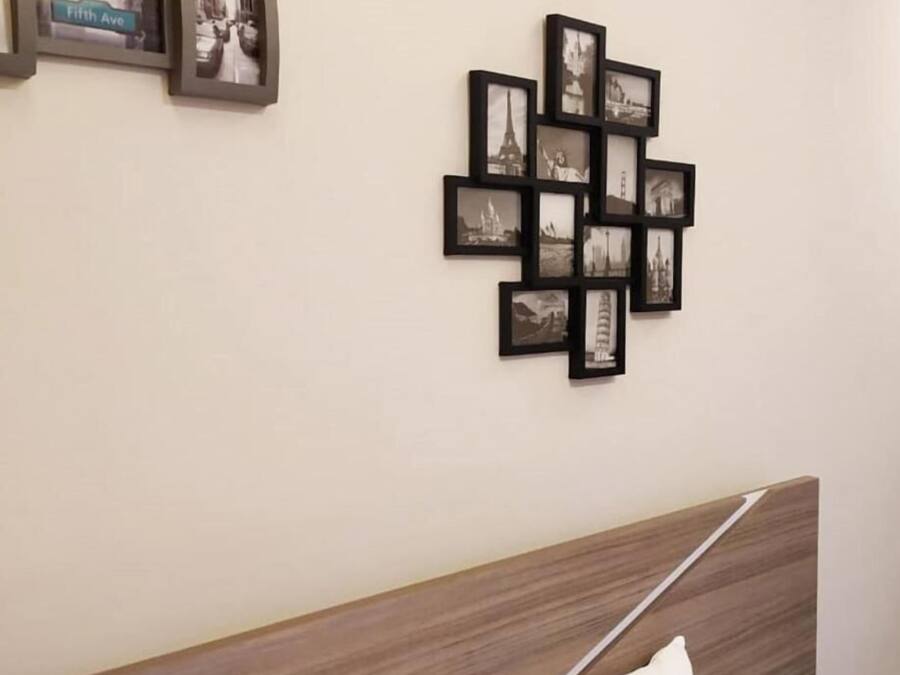 A bedroom with a wooden headboard, a white pillow, and a wall-mounted picture frame with multiple black photographs.