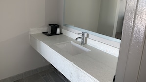 A bathroom with a white countertop, a sink, a mirror, and a black soap dispenser. - Super 8 by Wyndham Sulphur South (Sulphur)
