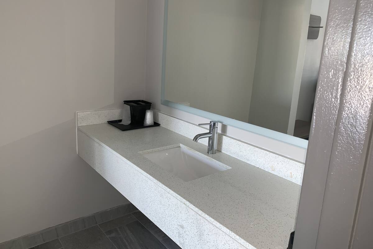 A bathroom with a white countertop, a sink, a mirror, and a black soap dispenser.