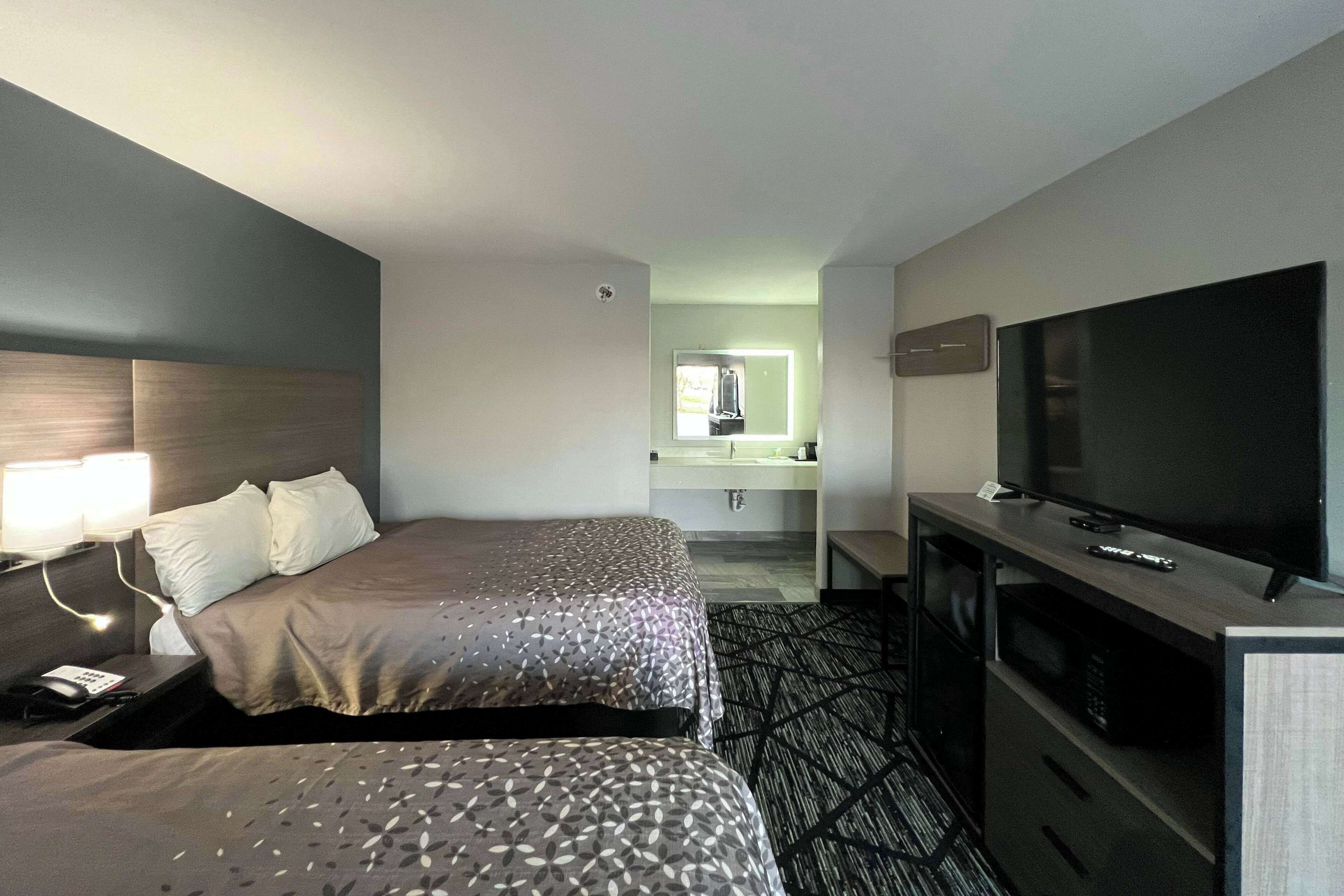 A hotel room with two beds, a TV, a desk, and a bathroom visible in the background.