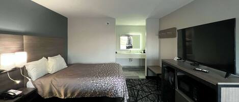A hotel room with two beds, a TV, a desk, and a bathroom visible in the background.