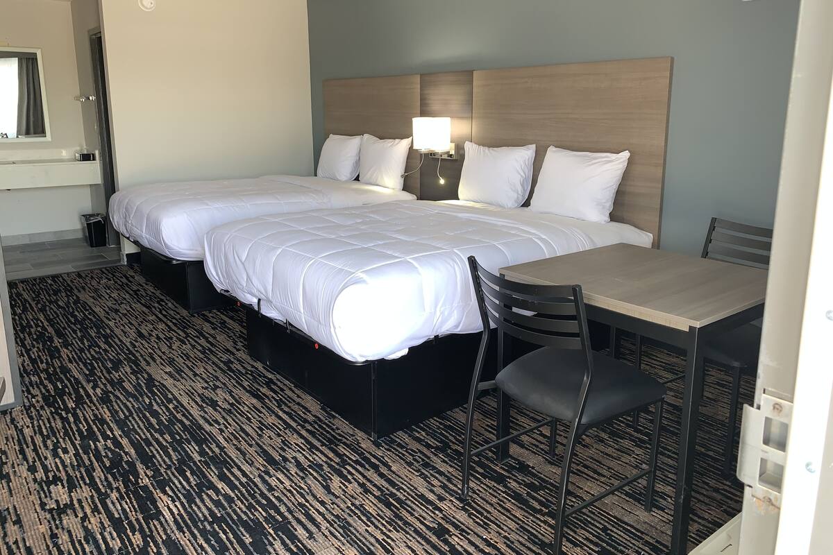 A hotel room with two beds, a desk, and a chair.
