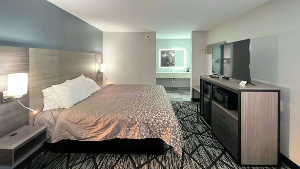 A hotel room with a bed, bedside table, lamp, TV, and a small desk with a mirror. - Super 8 by Wyndham Sulphur South (Sulphur)