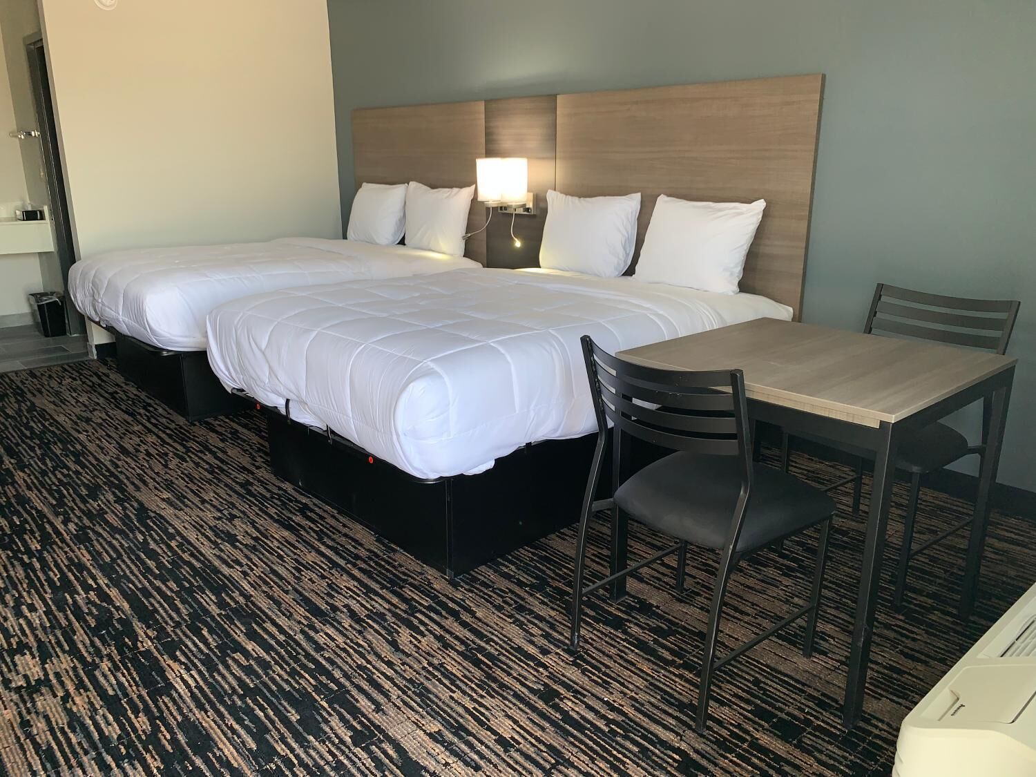 Habitación de hotel con dos camas, una mesita de noche, una silla y una pequeña mesa.