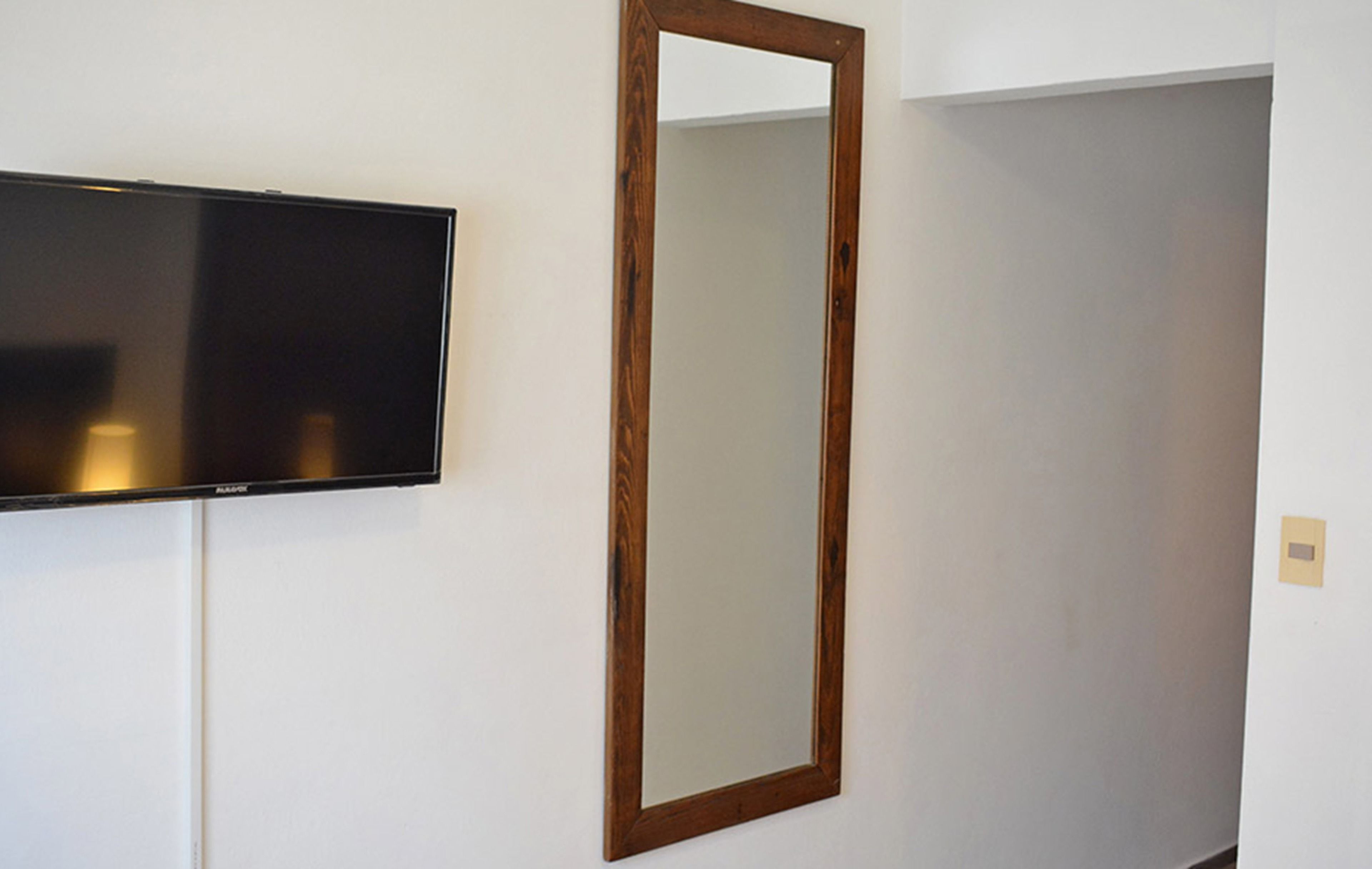Une chambre dotée d’un téléviseur à écran plat fixé au mur et d’un miroir encadré en bois.
