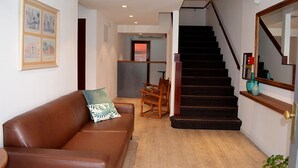 A living room with a brown leather sofa, a wooden chair, and a staircase leading to another room. - Hotel Express (Maldonado)