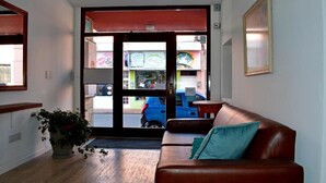 A lobby with a brown leather sofa, a potted plant, and a large glass door leading outside. - Hotel Express (Maldonado)
