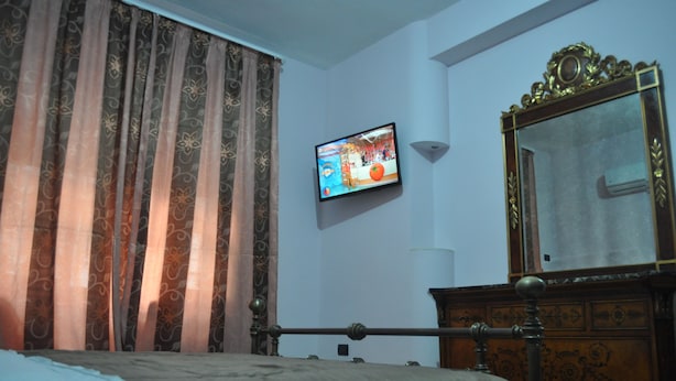 A bedroom with a bed, a television mounted on the wall, a mirror, and curtains. - Naples Experience B&B (Naples)