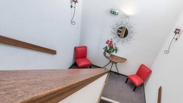 A staircase leading to a room with two red chairs, a small table with a plant, and a wall-mounted mirror.