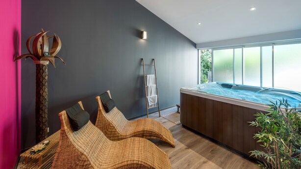 Une salle de spa moderne équipée d’un bain à remous, de chaises longues en osier et d’une échelle permettant d’y accéder.