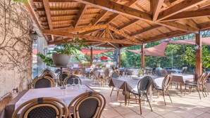 Une terrasse extérieure avec des tables et des chaises, recouverte d’un toit en bois et entourée de verdure.
