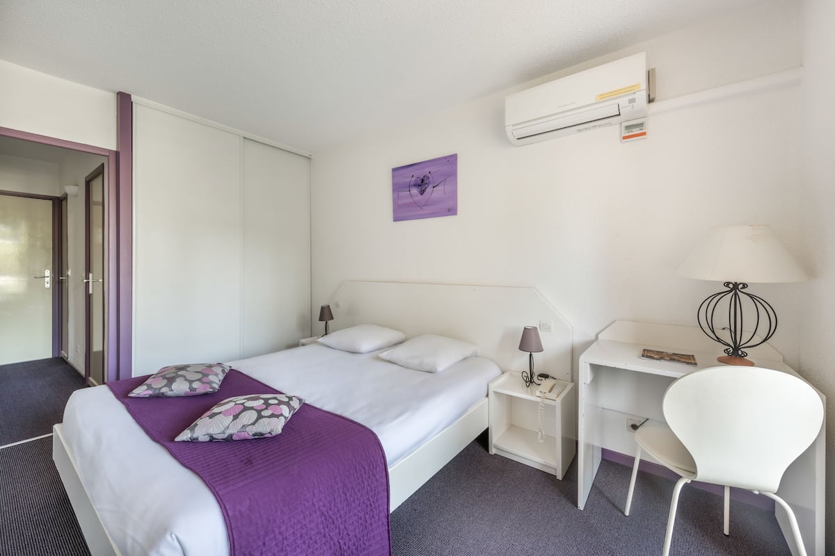 Une chambre d’hôtel équipée d’un lit, d’un bureau, d’une chaise, d’une lampe et d’un appareil de climatisation.