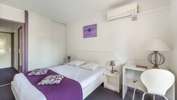 Una habitación de hotel con cama, escritorio, silla, lámpara y aire acondicionado.