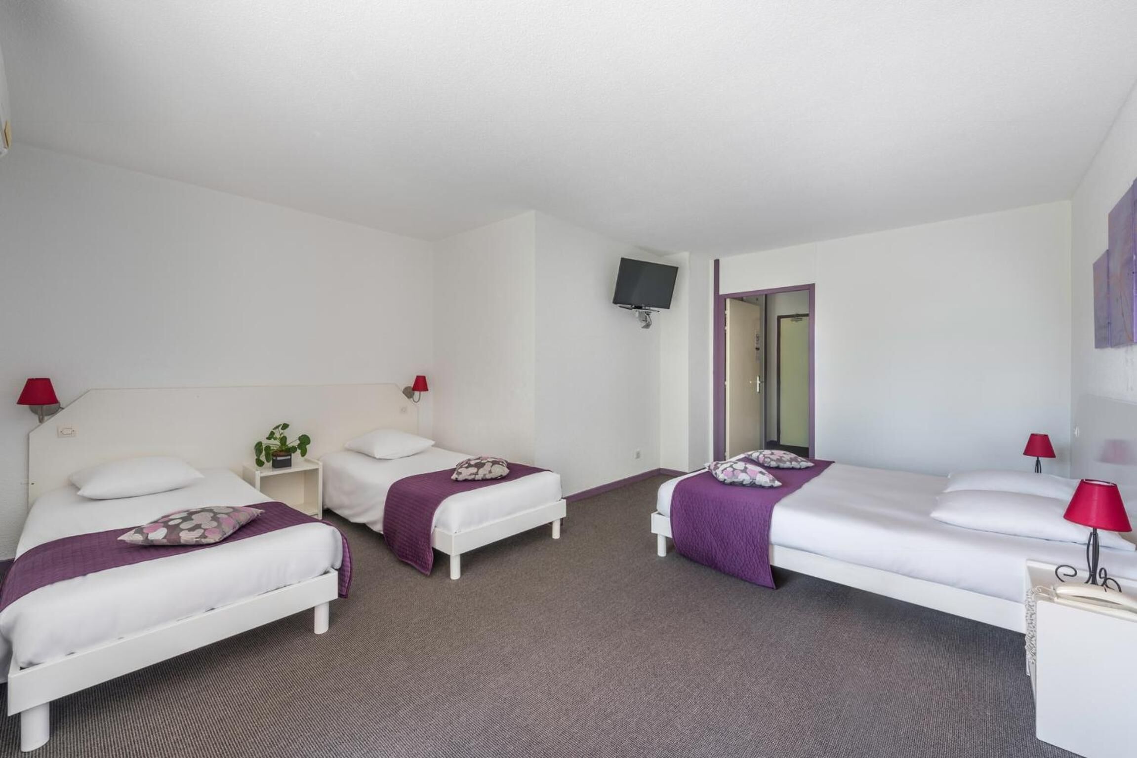 A hotel room with two single beds, a TV mounted on the wall, and a door leading to another room.