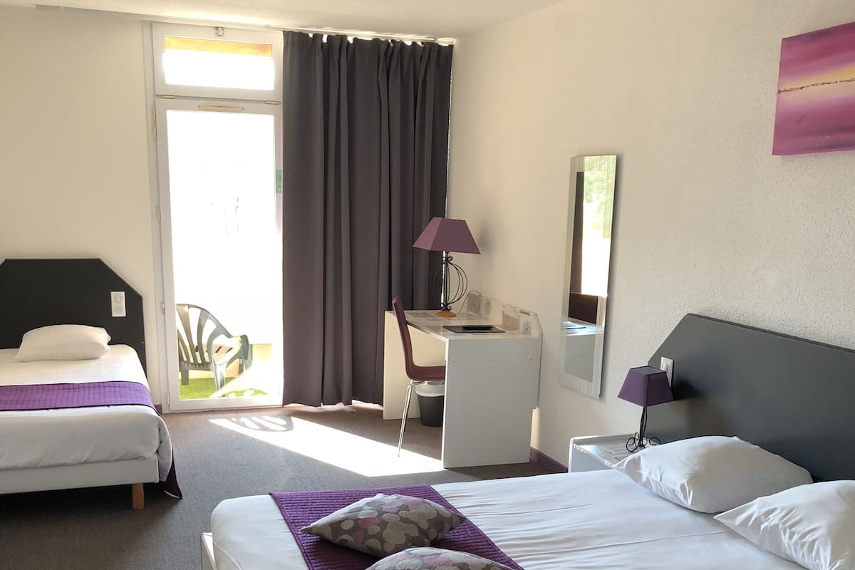 Une chambre d’hôtel avec deux lits, un bureau, une chaise, une lampe et une grande fenêtre avec des rideaux.