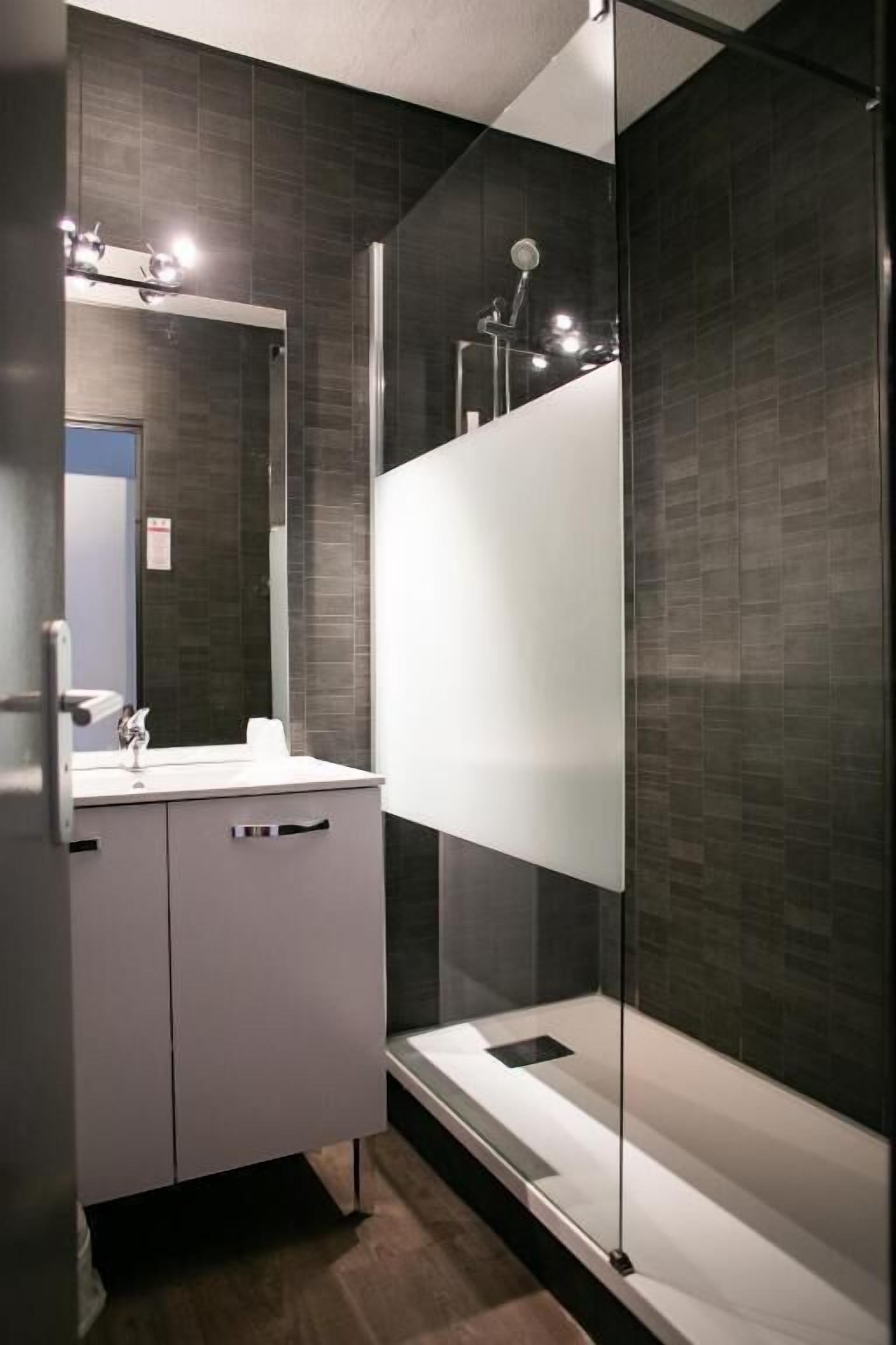 Un bagno moderno con cabina doccia in vetro, un mobile lavabo bianco e uno specchio sopra il lavandino.