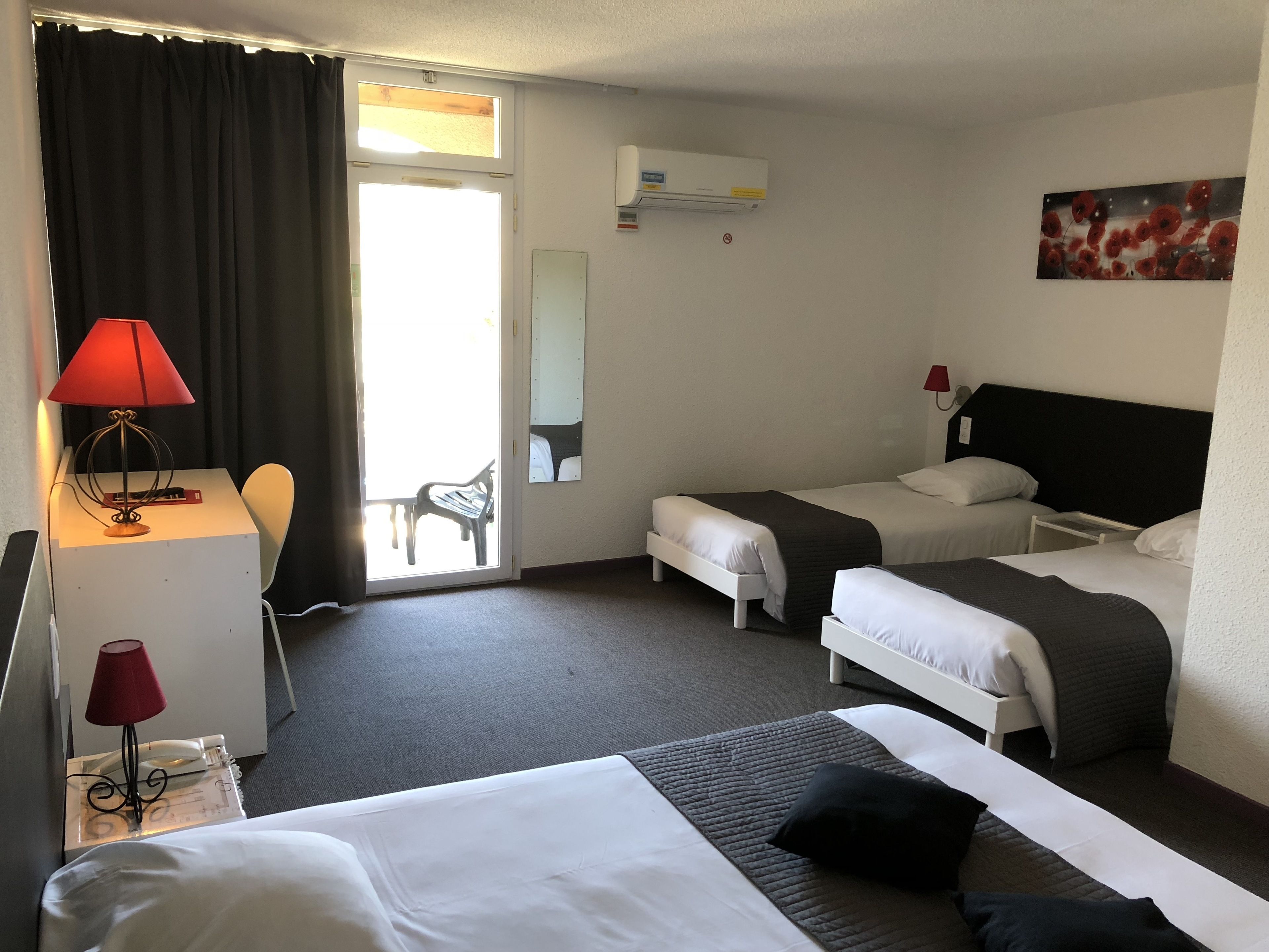 A hotel room with a bed, two bedside tables, a desk with a lamp, a chair, a sliding door to a balcony, and a painting on the wall.