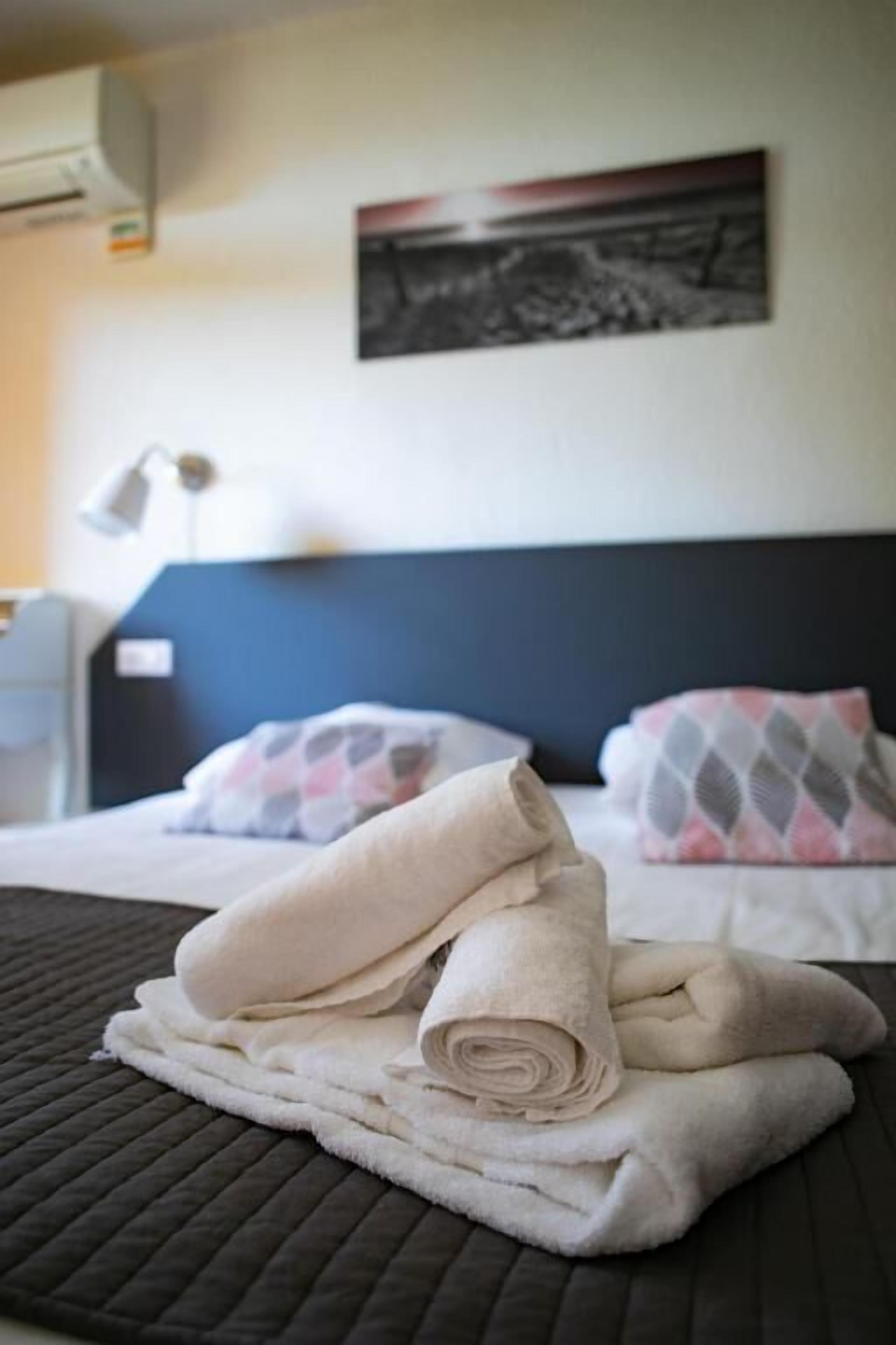 Un lit bien fait, avec des serviettes pliées, une tête de lit sombre et un climatiseur fixé au mur.