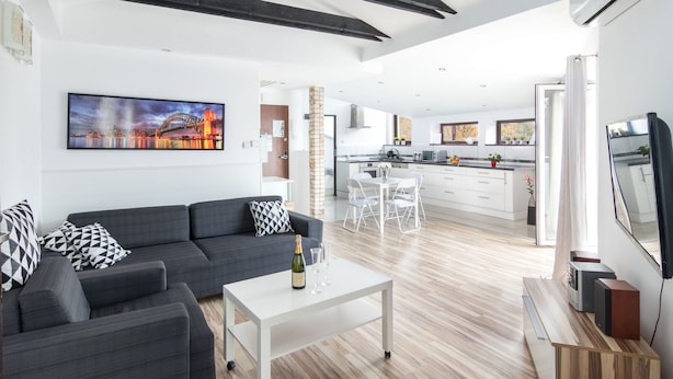 A modern living room with a sofa, a coffee table with a bottle and glasses, a TV, and a kitchen in the background. - Station Apartments Kątowa 11 Krakow (Kraków)