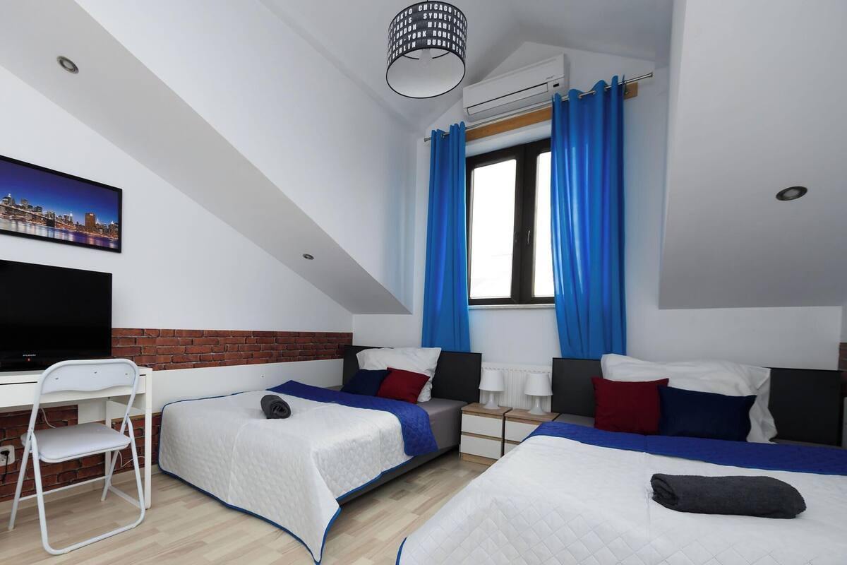 Habitación de hotel con televisión, dos camas, escritorio, silla y ventana con cortinas.