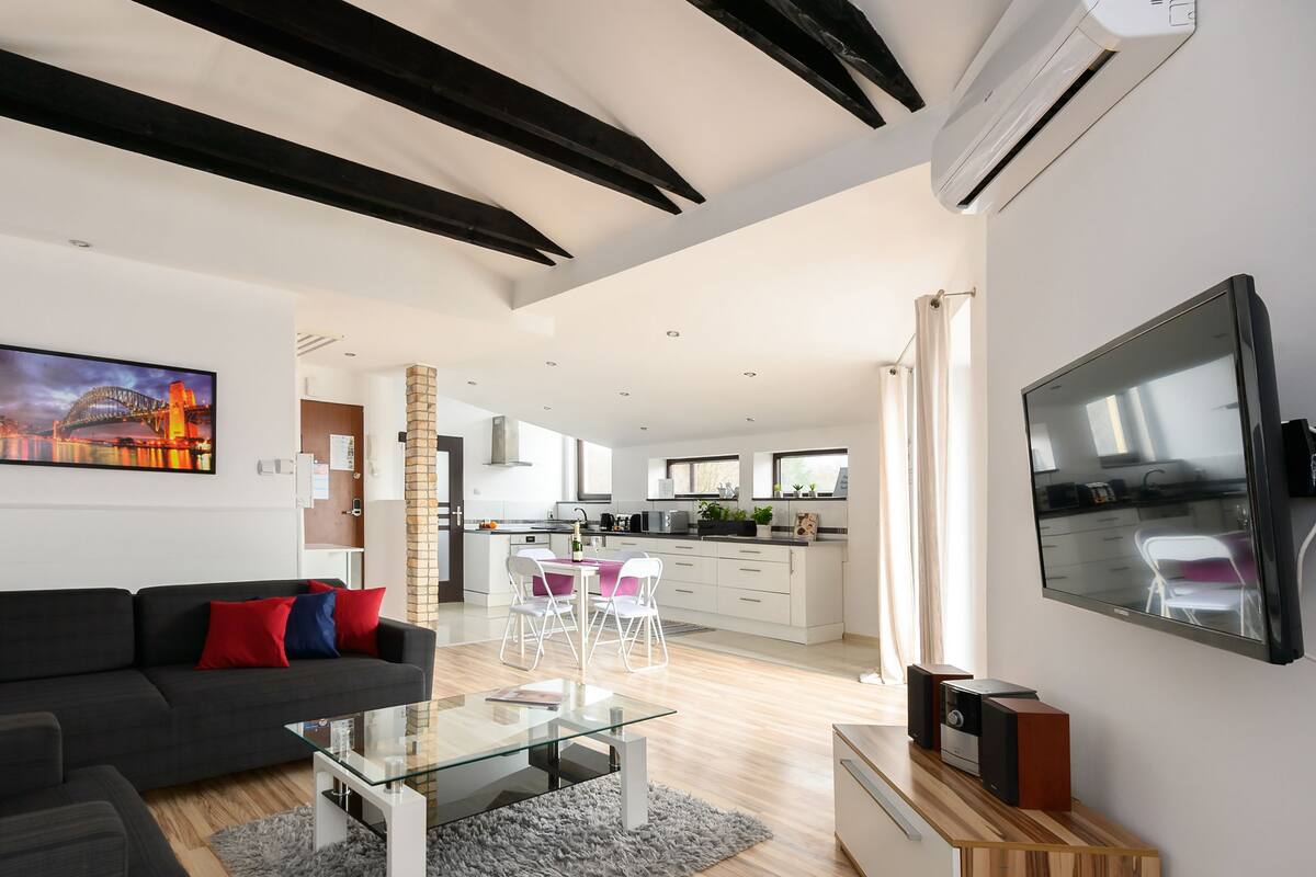 Una sala de estar moderna con un sofá oscuro, una mesa de centro de vidrio y un televisor de pantalla plana.