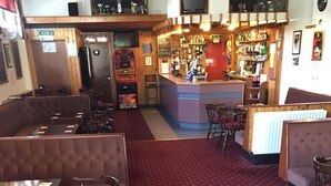 Un restaurant avec des banquettes, des tables et des chaises. Il y a un bar avec un comptoir et des étagères remplies de bouteilles.