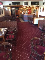 Un restaurante con cabinas, mesas y sillas. Cuenta con una zona de bar con mostrador y estantes llenos de botellas.