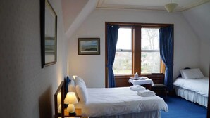 Une chambre d’hôtel avec un lit simple, une table de chevet avec une lampe, une fenêtre avec des rideaux et un tableau encadré au mur.