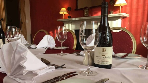 Une table à manger dressée avec des verres à vin, une bouteille de vin et des couverts.