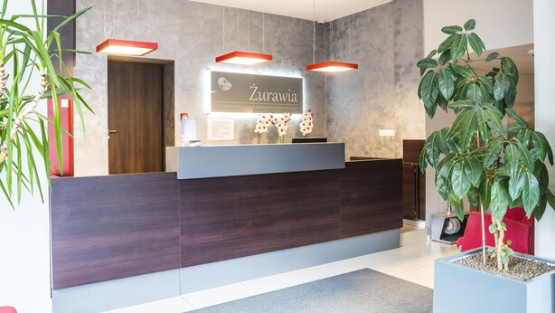 A reception area with a dark wood reception desk, a sign reading "Zurawia," and a large potted plant. - Centrum Scsk Zurawia (Warsaw)