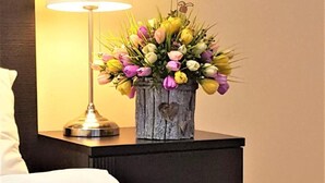 A neatly made bed with a white towel, a wooden nightstand with a lamp, and a vase of flowers. - Centrum Scsk Zurawia (Warsaw)