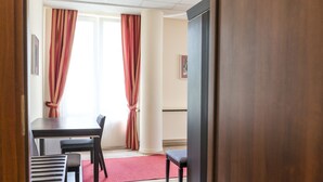 A room with a wooden table, two chairs, a red rug, and a large window with red curtains. - Centrum Scsk Zurawia (Warsaw)