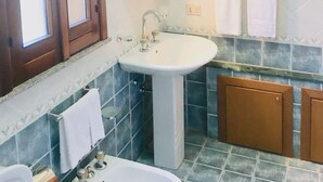 Un baño con un lavamanos blanco, un espejo encima y una ventana con marcos de madera. Hay dos toallas colgadas en un perchero y un mueble de madera debajo del lavamanos.