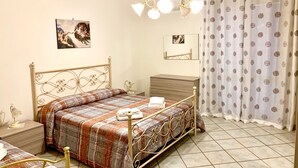 Un dormitorio con estructura de cama metálica, una mesita de noche con lámpara, un aparador y un espejo.