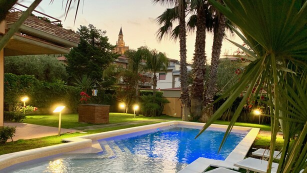 Una piscina al aire libre con sillones de descanso, rodeada de palmeras y un jardín bien iluminado.