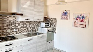Una cocina moderna con estufa a gas, lavaplatos de acero inoxidable y armarios blancos. Hay un microondas y un lavavajillas en la encimera.
