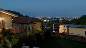 Una azotea con sillones de sol, una piscina y vistas a un paisaje urbano al anochecer.