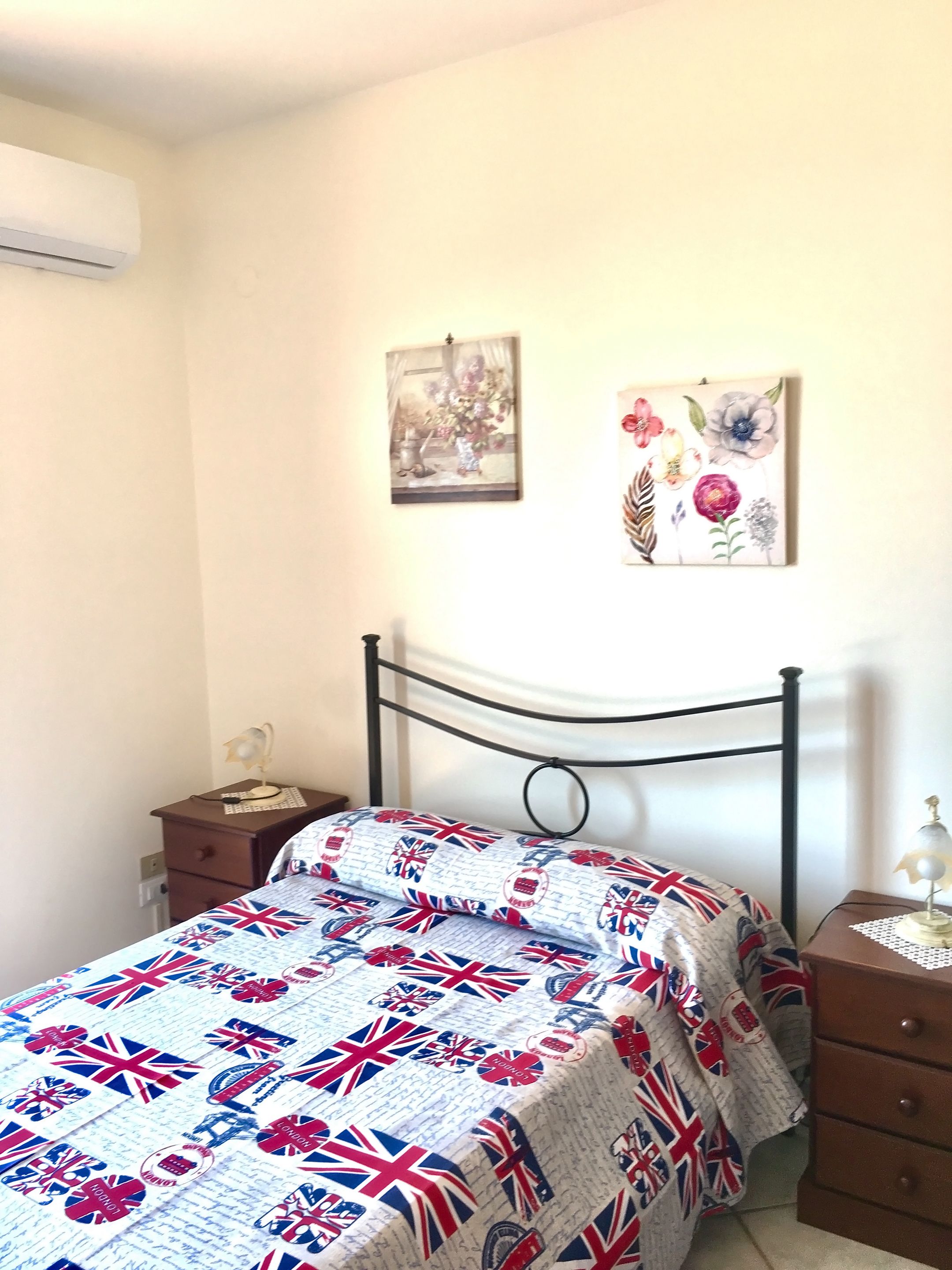 Une chambre à coucher comprenant un lit, une table de chevet, une lampe et deux œuvres d’art murales.