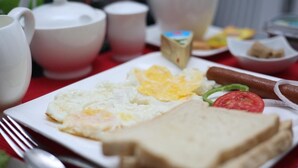 Ein Frühstücksteller mit Eiern, Toast, einer Tomate und einer Wurst.
