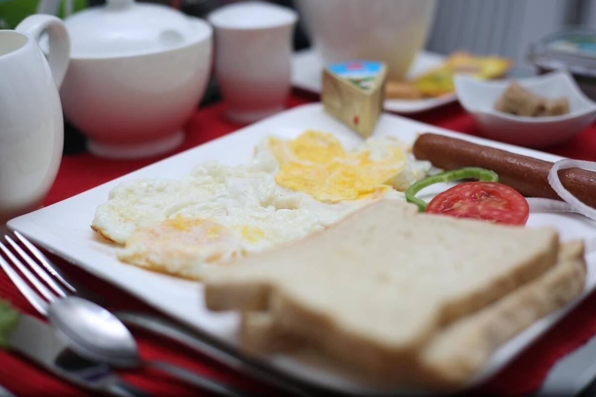 A breakfast plate with eggs, toast, a tomato, and a sausage.