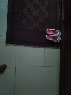 A pair of pink slippers on a patterned rug, a tiled floor, and a person's foot. - Kingsby homes and hotel (Accra)