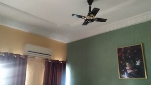 Ein Zimmer mit Deckenventilator, Klimaanlage, einem fenster mit Vorhängen und einem gerahmten Bild an der Wand.