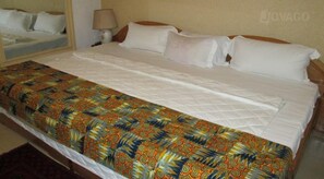 A hotel room with a bed, a nightstand, and a lamp. - Kingsby homes and hotel (Accra)