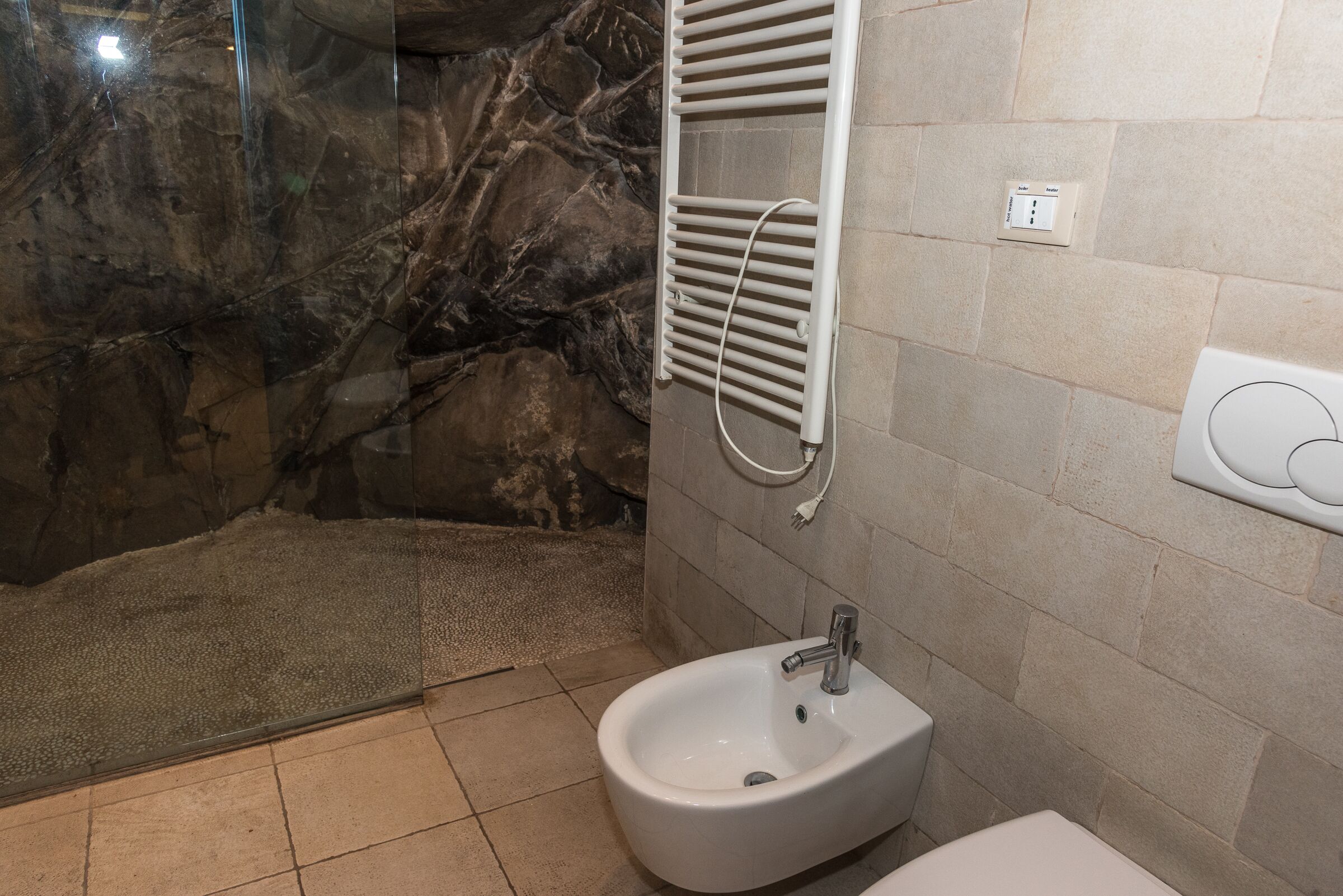 Une salle de bain équipée d’un bidet, d’un porte-serviettes et d’un espace douche avec une porte en verre.