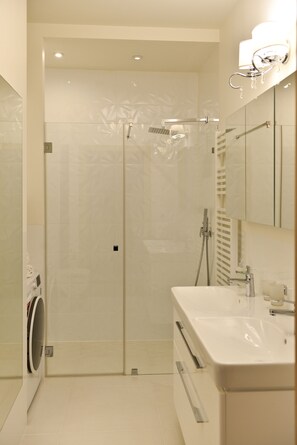 Un baño moderno con ducha de vidrio, lavamanos blanco y espejo sobre el lavamanos.