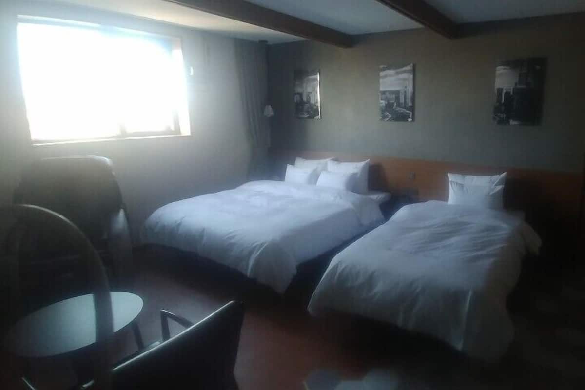 A hotel room with two beds, a small table, and a chair.
