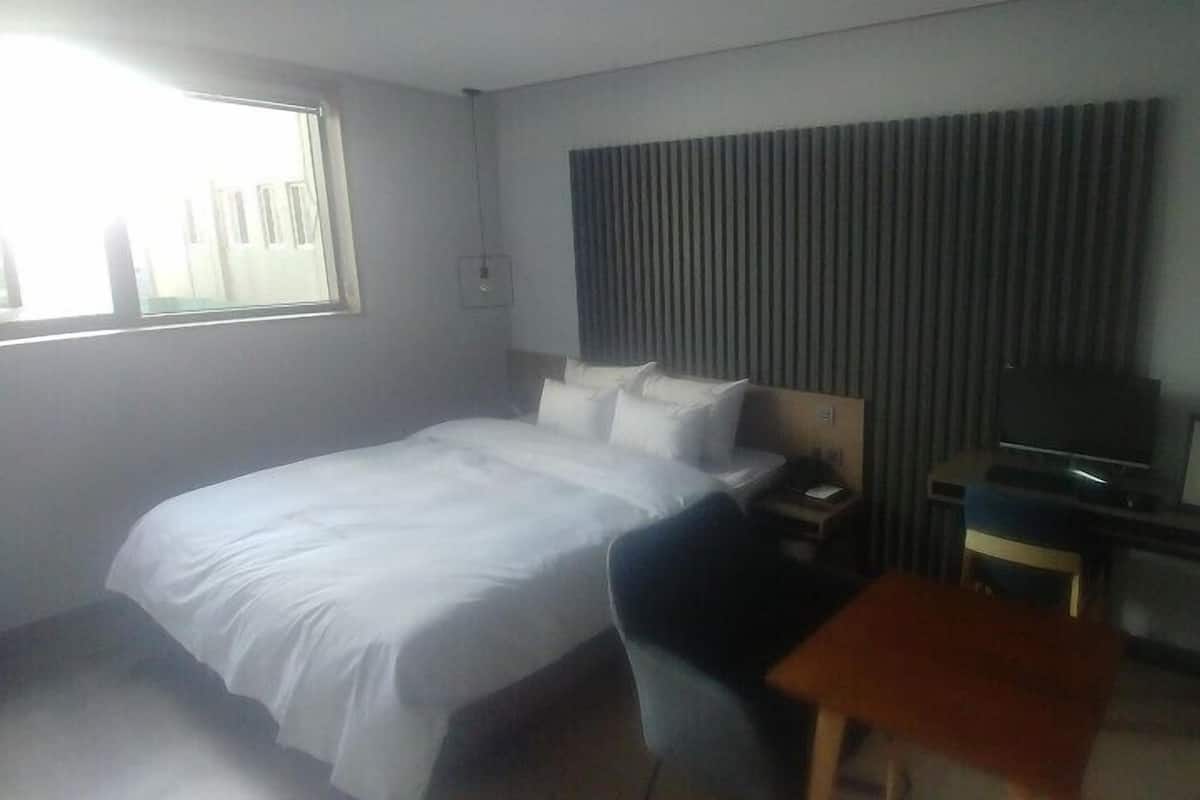 A hotel room with a bed, a desk, a chair, a television, and a window.