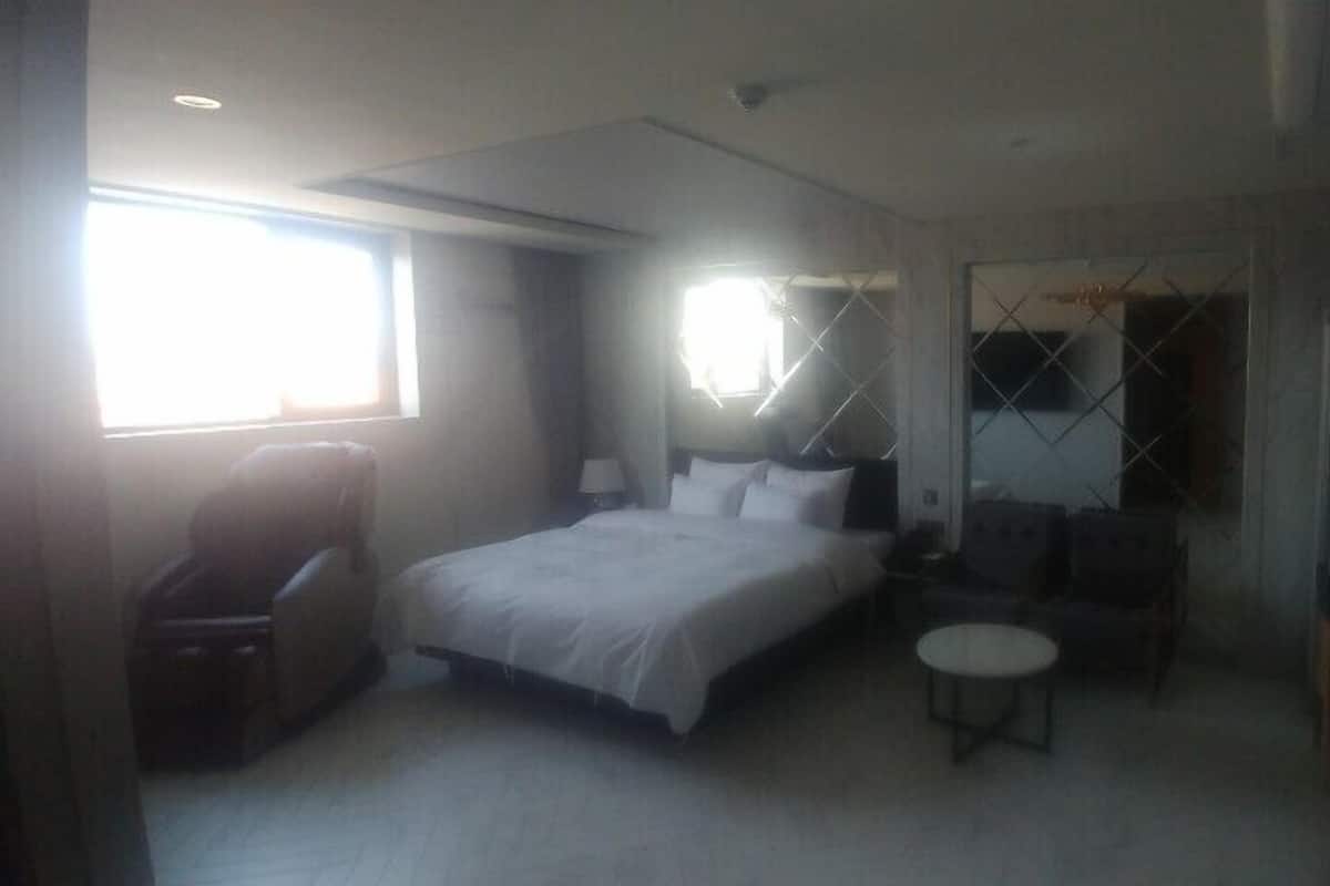 A hotel room with a bed, a chair, a small table, and a wardrobe.