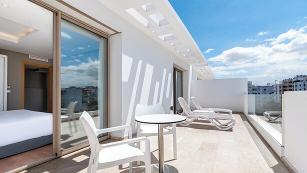 Un balcon moderne avec un lit, deux fauteuils et une table.